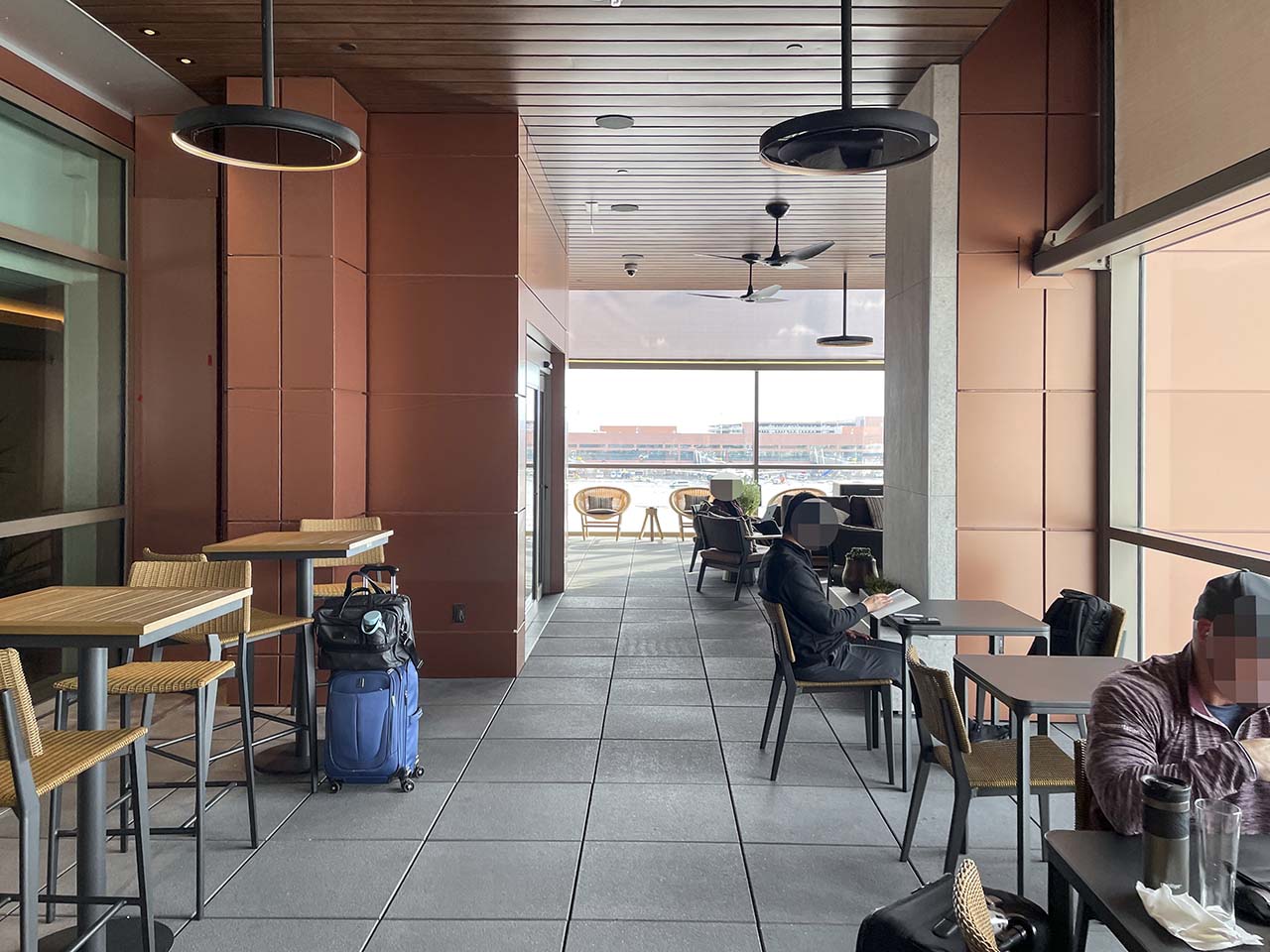 Tables and chairs next to large windows in the terrace at the SLC Amex Lounge